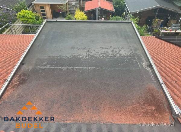 Verouderd plat dak met slijtage tussen schuine daken in Budel